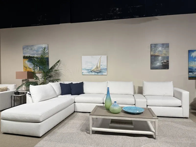 Bassett Beckham sectional (model 2676), a white chaise sectional shown with navy accent pillows, a wood-top coffee table and coastal sailboat art on The Sofa Store showroom floor